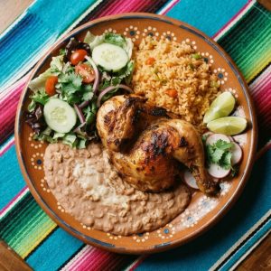 Grilled chicken with Mexican rice, refried beans and a green salad, on a terracotta clay plate.